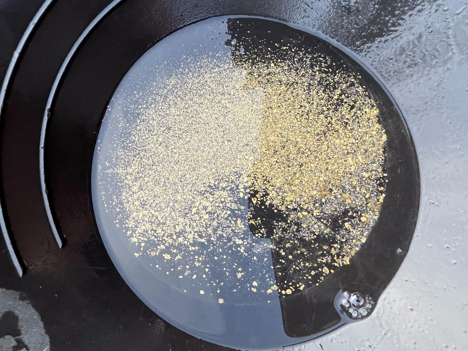 A black gold pan full of fine yellow gold concentrate, dry.