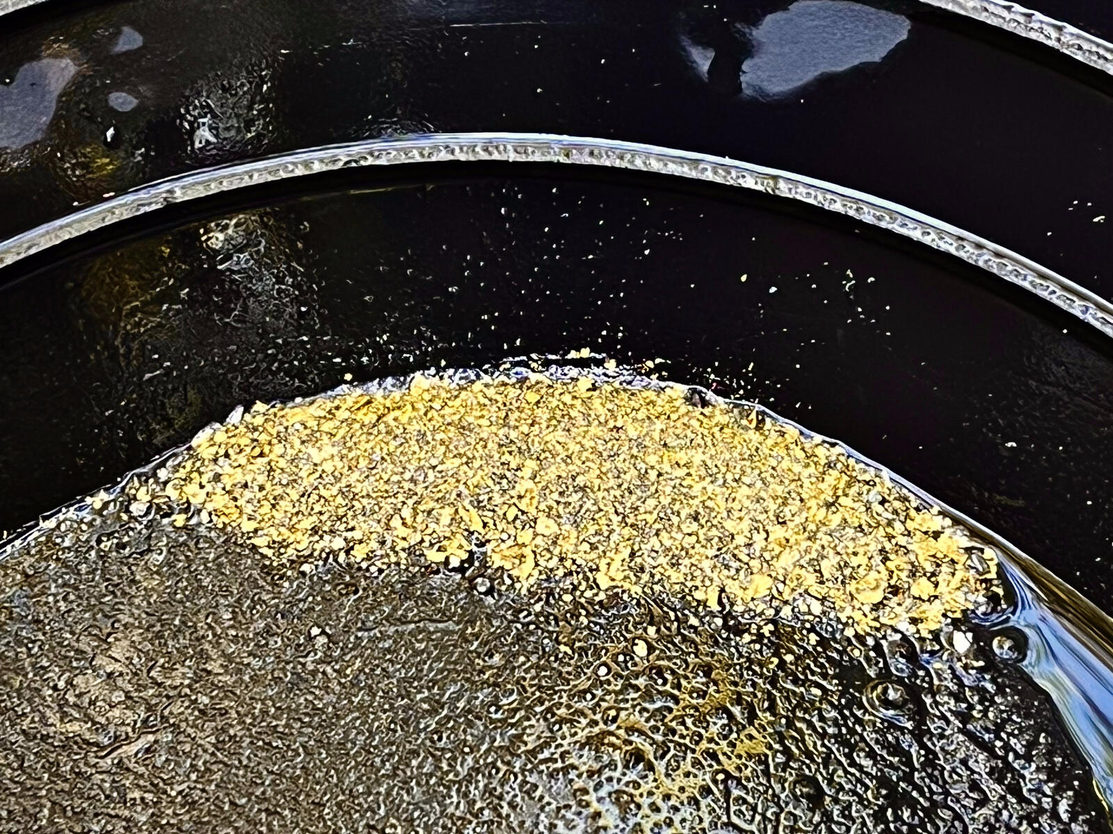 A bed of larger gold flakes settled in the bottom of a wet pan.