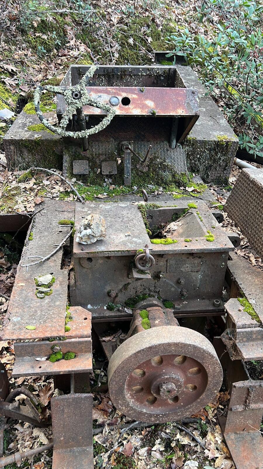 A rusted Williams Patent Crusher and Pulverizer hammer mill bolted to a car chassis, partly covered by moss, still on the Red Wing property.