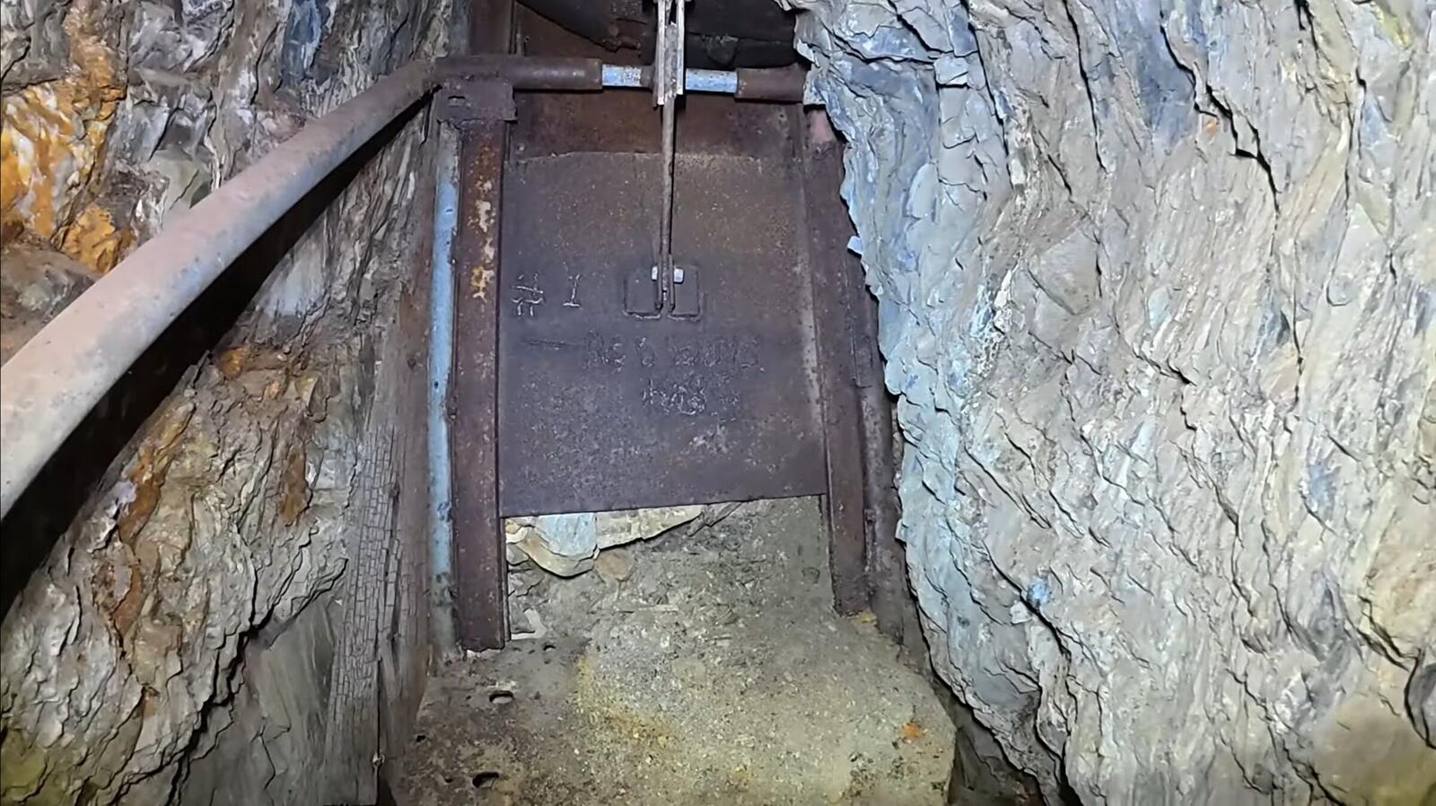 An iron ore-chute door inside the Red Wing workings, set in a wooden frame above the drift, with iron rails on the floor leading up to it.