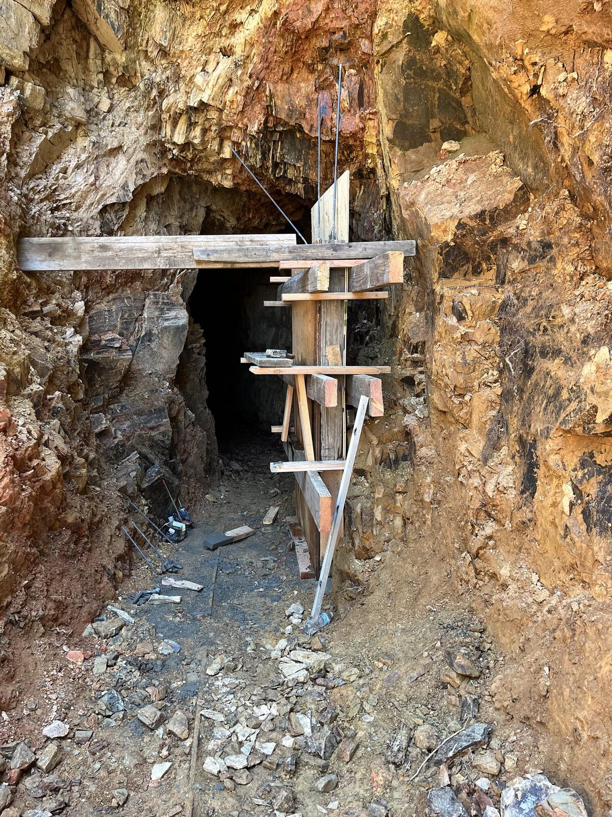 The wooden form built for the new concrete portal at the Red Wing, with heavy verticals, cross-bracing, span beams, and tie-back cables anchored into the rock; the deeper working visible through the form.