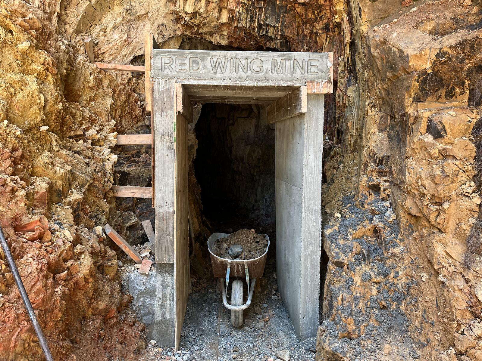 The new concrete portal at the Red Wing, with RED WING MINE cast in mirror image into the wooden lettering board still set inside the form; a heavy mason's hammer rests on the cap beam above the dark portal opening.